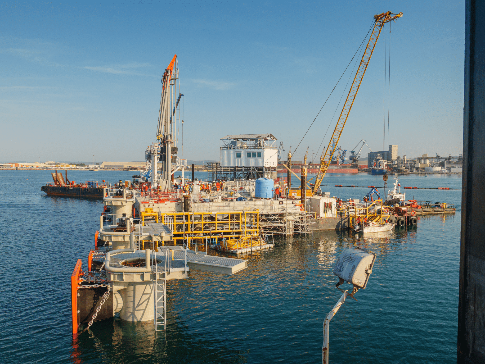 Vue d’un chantier maritime montrant une plateforme de construction flottante avec des grues, des équipements de levage et des ouvriers, au port de Sète-Frontignan.
