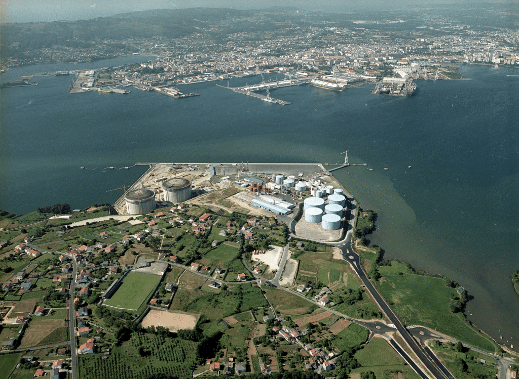 Vue aérienne d’un site industriel en bord d’estuaire avec plusieurs réservoirs cylindriques, des bâtiments techniques, un quai portuaire et des zones résidentielles et agricoles autour.